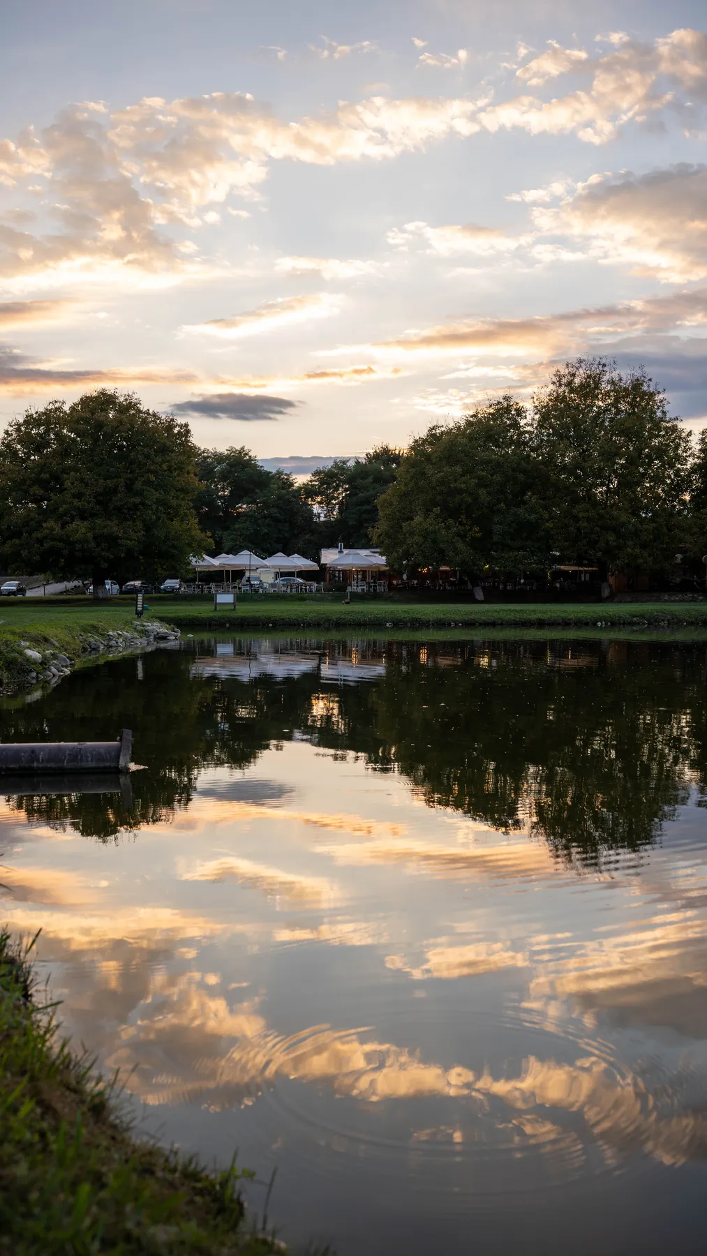 Norii apusului reflectați în lac, cu restaurantul între copaci